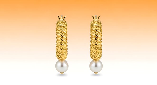 Pair of elegant gold hoop earrings with white pearls hanging from them on orange background