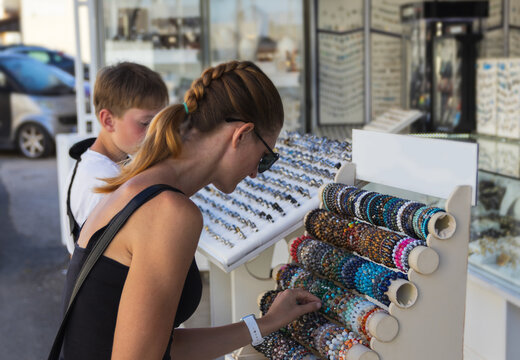 Side view of a mother and her son looking at a display of colorful handmade bracelets outside a local souvenir shop during a summer vacation in Kato Gouves, Crete