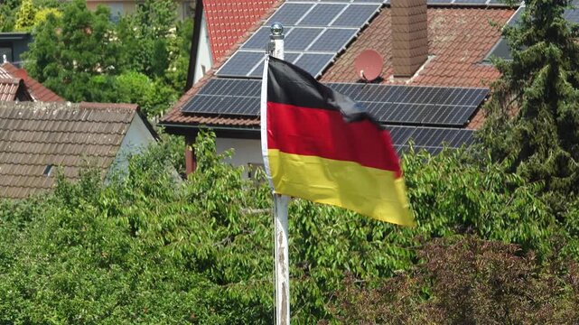 Eine Deutschlandfahne an einem Fahnenmast weht im Wind, mit Solard&auml;chern im Hintergrund