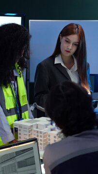 Female architect and engineer examine building model. Diverse corporate team using tablet and collaborating on development project at the office