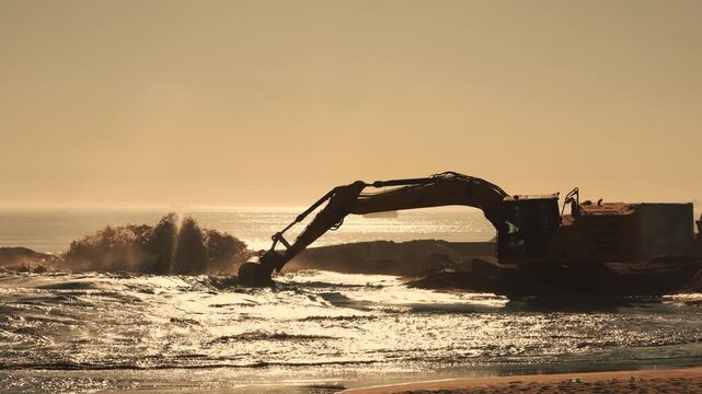 Excavator working on beach dredging sand at sunrise