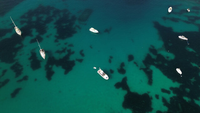 Aerial view of several sailboats and motorboats anchored in the clear turquoise waters of the Mediterranean Sea off the coast of Malta.