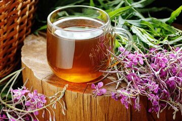 Fermented willow herb tea in a cup with fresh fireweed flowers on rustic wooden background © spiegelka