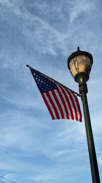 American flag attached to a lamp post blows in the wind against an early evening sky with copy space