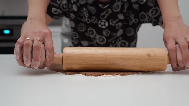 Mother helps son roll out gingerbread dough with wooden rolling pin on kitchen table. Family cooking education, parent child baking holiday sweet cookie recipe together inside home kitchen.