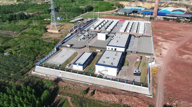 Aerial view of a substation with transformers and industrial buildings surrounded by fences and power infrastructure