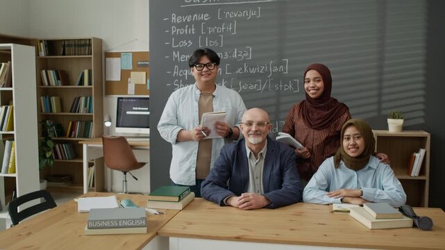 Portrait of Caucasian senior male teacher and diverse young adult migrant students smiling in classroom. Footage is ideal for promoting inclusive business language courses and adult education programs