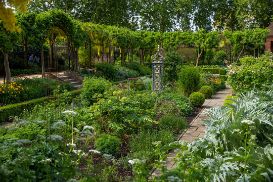 A vibrant formal garden pathway at Kew botanical gardens with lush greenery, yellow laburnum arches, and decorative elements.