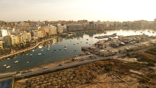 Aerial view of the marina in Msida with numerous boats moored in the harbor, surrounded by urban buildings and coastal roads under the warm light in Malta.