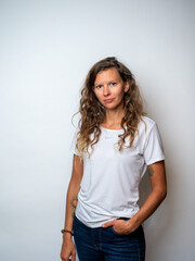 Fototapeta premium Studio portrait of a mid-thirties woman on a white backdrop wearing a white t-shirt and dark blue jeans, with dark blonde wavy hair and a relaxed, natural expression.