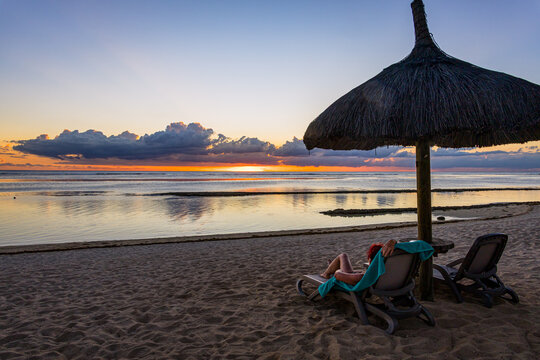 Femme allong&eacute;e sur un transat devant le couch&eacute; de soleil sur une plage au Nord-Ouest de l'Ile Maurice, Oc&eacute;an Indien, Afrique