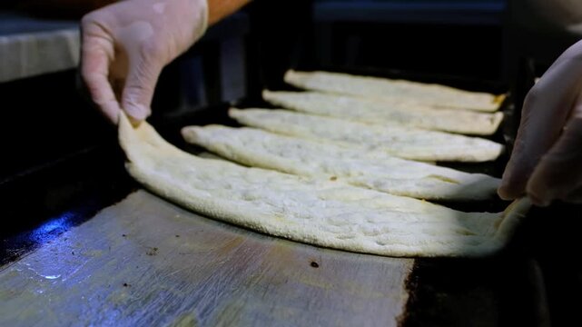 Prepared pides lined up on black baking trays in a bakery kitchen, ready for the oven. Food production, tray arrangement, baking preparation and professional kitchen workflow concept.