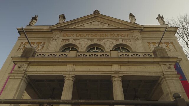Neoclassical facade of the historic Prinzregententheater in Munich Germany, decorated with stone statues on the roof and housing a giant amphitheatre stadium seating inside.
