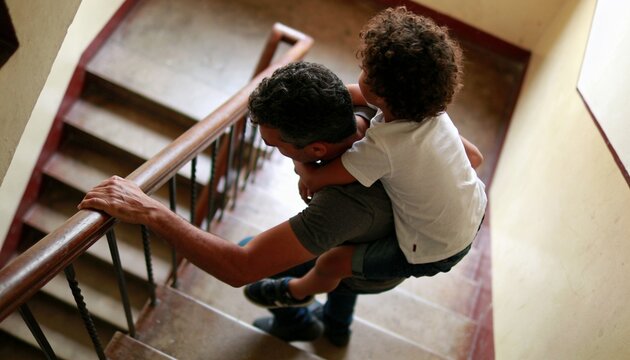 Father and Son Bonding on Staircase: A loving father carries his young son on his back as they ascend a staircase, sharing a moment of connection and togetherness.