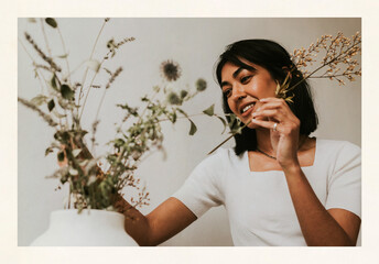 Obraz premium Woman arranging dried flowers in white vase indoors