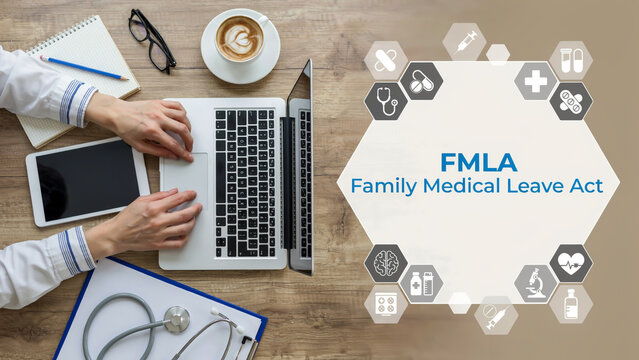 A person's hands on a laptop and documents about FMLA Family Medical Leave Act on a wooden desk