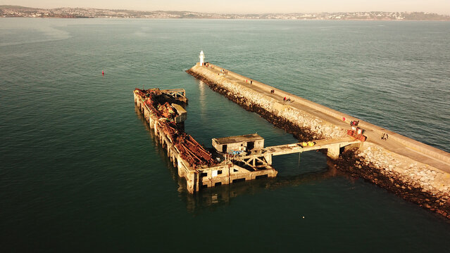 Aerial view of the historic Brixham Breakwater and the derelict old pier structure extending into the sea, with people walking on the breakwater in Brixham, England, United Kingdom.