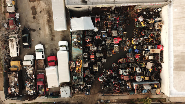Aerial view of an industrial scrap yard filled with various vehicles, machinery, and piles of metal parts in an urban setting in Los Angeles, California, United States.
