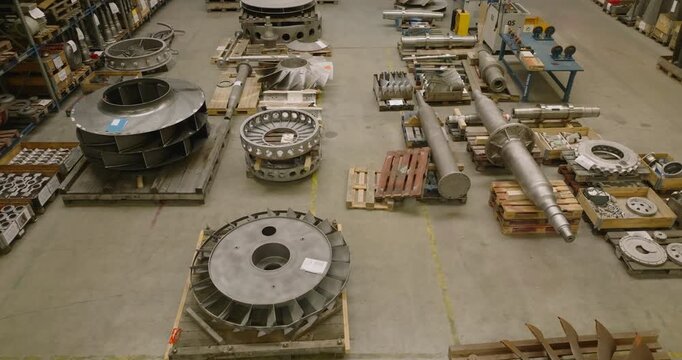 High angle view of various heavy metal turbine components arranged on wooden pallets in a warehouse