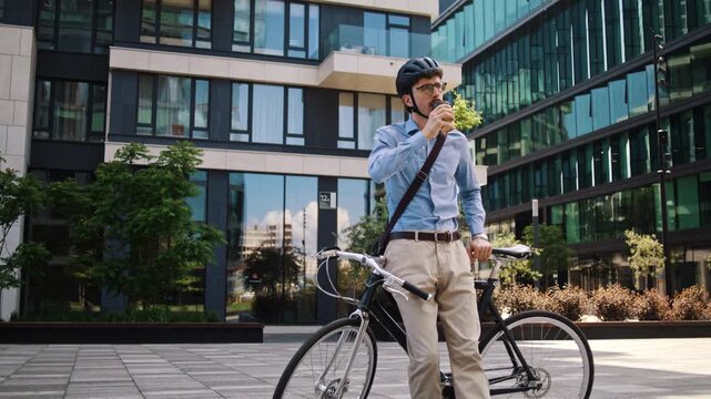 Man waits leaning on bicycle with coffee cup by office building