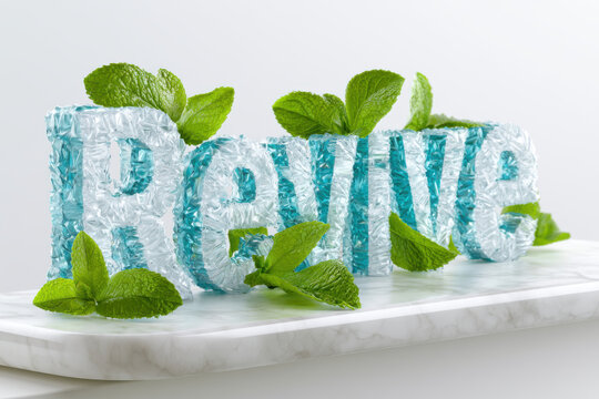 Minty Refreshing Revive - The word "Revive" is intricately sculpted from textured chunks of clear ice and crystalline blue shards, decorated with vibrant green mint leaves on a white marble slab