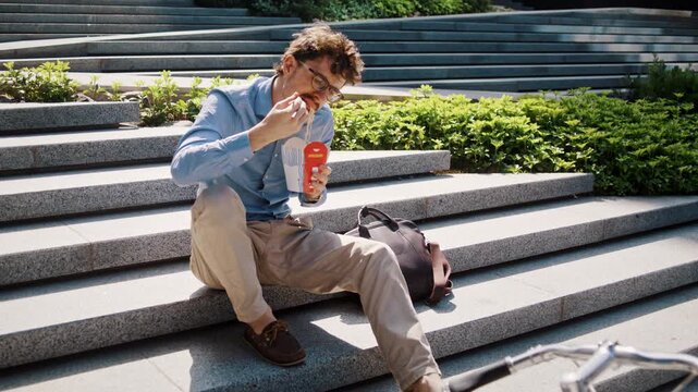 Man eats lunch near backpack on sunny office steps alone