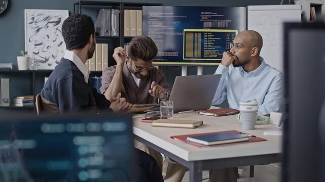Handheld shot of multiethnic young IT professionals discussing coding issues during brainstroming meeting in office. Video suitable for technology marketing and IT corporate campaigns