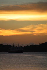 Obraz premium Golden Sunset Seascape with Ship Silhouette and Ocean Reflection