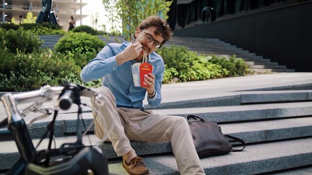 Man in glasses eats lunch behind bicycle on city office steps