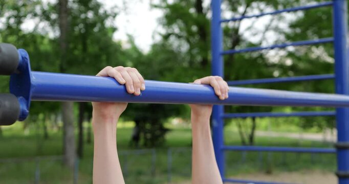Close-up of childs hands gripping pull-up bar during outdoor workout on sports playground. Active lifestyle scene captures strength training, effort and healthy childhood activity.