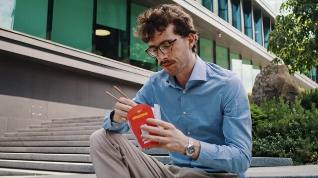 Man eats noodles on office steps near parked bicycle alone