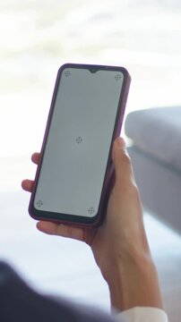 Vertical video: Adjusting person holding phone in purple case on sofa, responding to crosshair