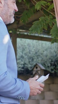 Vertical video: Camera pulling back man in blue suit holding notes at pergola preparing, copy space