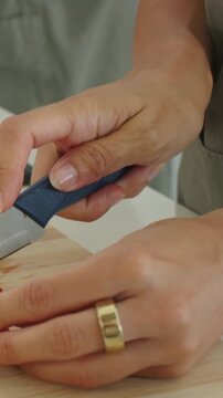 Vertical video: Slicing hands wearing apron preparing halved strawberry on board using blue knife