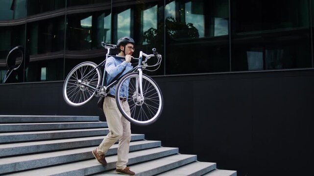 Man carries bicycle downstairs near dark glass office building
