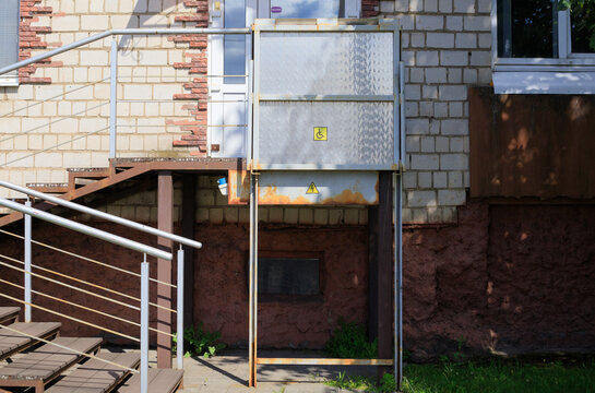 Outdoor wheelchair platform lift for disabled people, accessible metal elevator structure near building stairs under blue sky