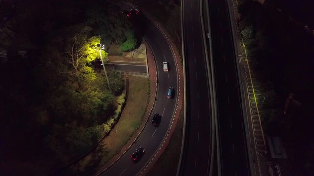 Near-vertical aerial view looking straight down at one of the curved cloverleaf ramps of the Semanggi Interchange in Jakarta, Indonesia, at night.