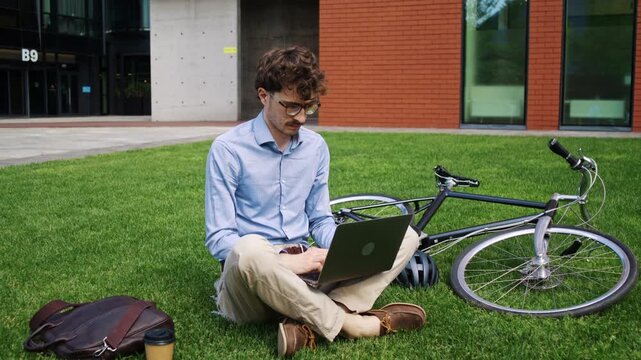 Office man works on laptop near bicycle on sunny office grass