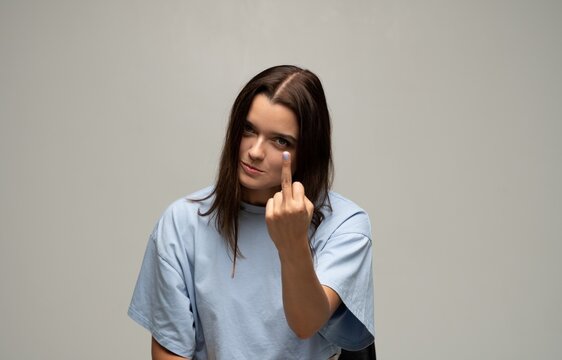 Young woman showing middle finger gesture expressing anger, defiance, and rebellion on a simple background