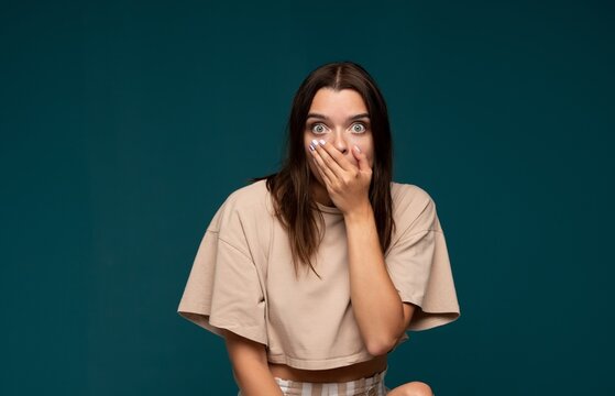 Young woman covering mouth with hand, having wide eyes, experiencing shock, surprise, and disbelief