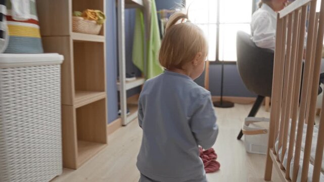 Toddler girl holding mesh laundry basket and reaching with hand beside crib inside residential building; curiosity exploration.