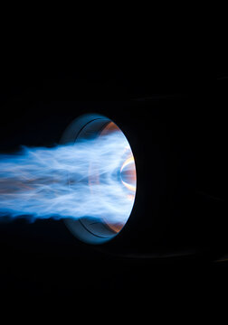 Powerful blue flame thrusting from a jet engine nozzle against a dark background, illustrating combustion and propulsion.