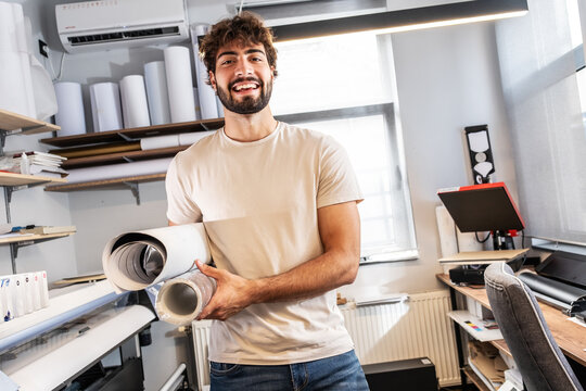 A print shop worker stands confidently in the production area, surrounded by printing equipment and materials. The portrait highlights professionalism, experience, and dedication to quality work.