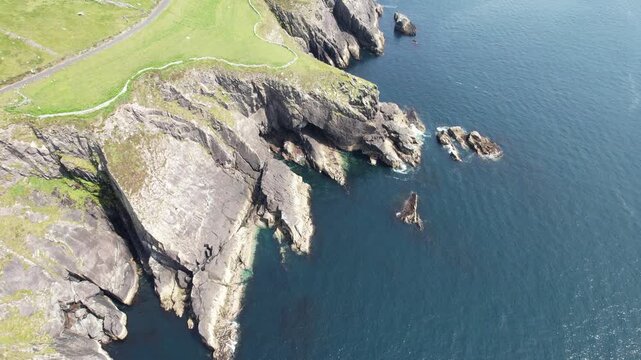 Drope aerial, 4k high altitude aerial shot flying backward over dramatic, rugged cliffs and deep blue ocean waters along rocky coastline Dingle Peninsula ireland