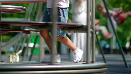Young boy inside spinning playground carousel while ride turns quickly with children swinging in background, energetic park scene expressing motion excitement and lively childhood play © Marco