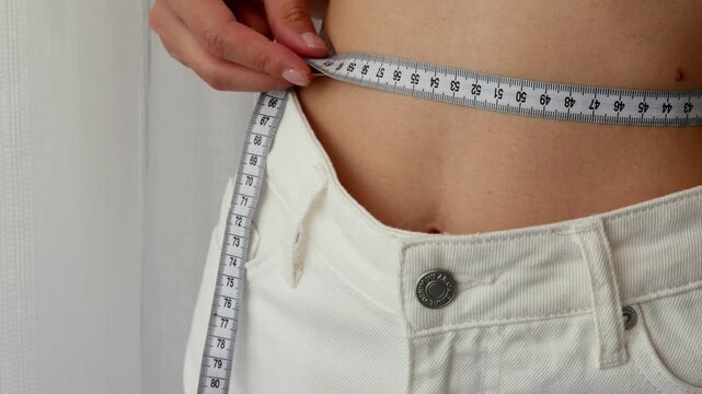 Woman measuring waist with tape showing body transformation and weight loss progress concept.