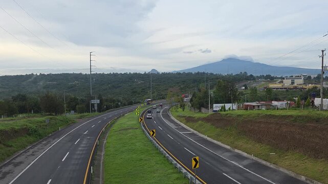 Vista a&eacute;rea en &aacute;ngulo picado de carretera con tr&aacute;fico bidireccional y monta&ntilde;as al fondo en d&iacute;a nublado