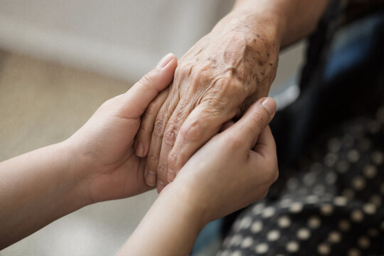 Young person holding senior elderly hand in supportive gesture

