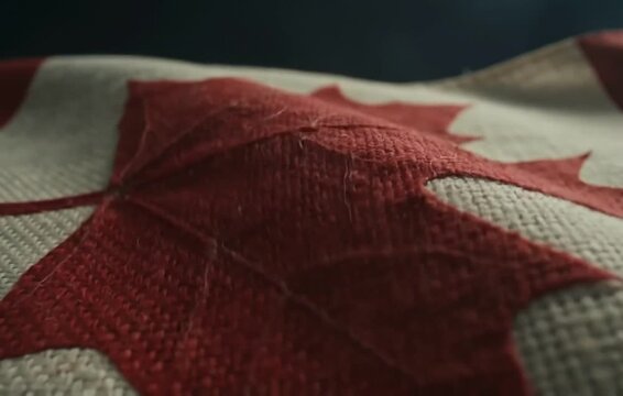 Close-up of Canadian flag fabric texture with red maple leaf symbol against dark background, detailed view.