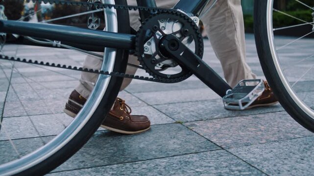 Man in moccasins pushes bicycle across office pavement close view